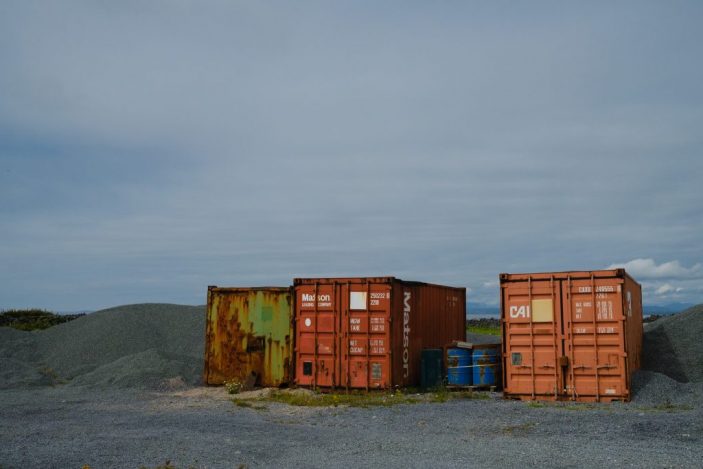 3 containers colorés, entourés de tas de graviers gris sous le ciel gris